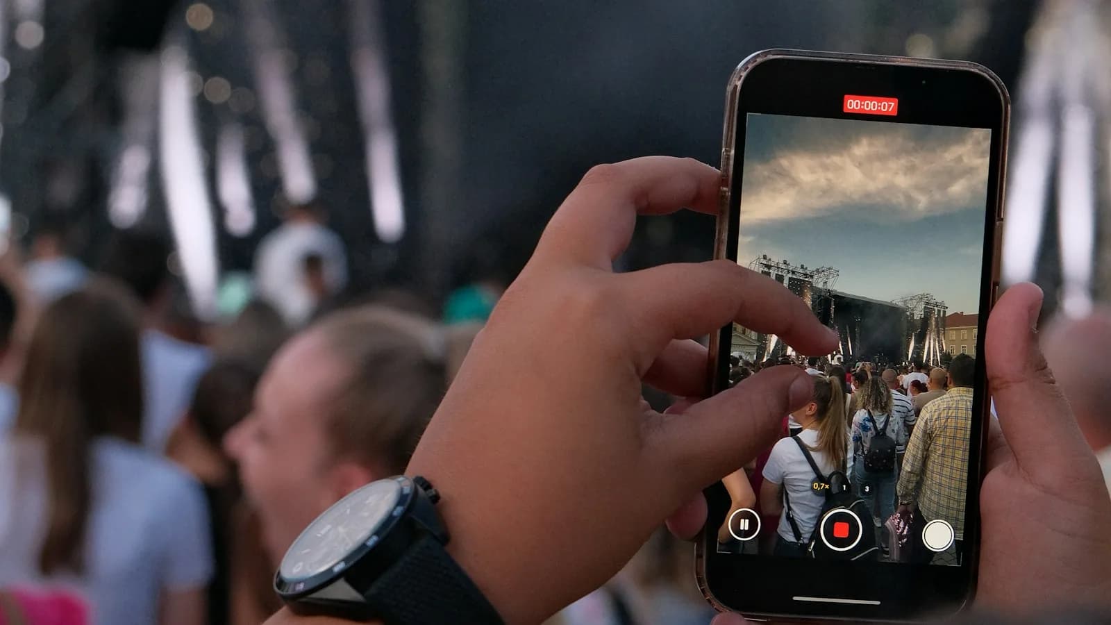 Dans le public, une main enregistre un concert sur l'écran d'un téléphone : l'image que la salle relaie.